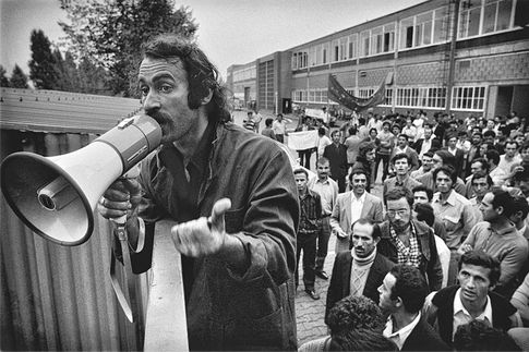 Baha Targün mit Megafon am Werkstor, im Hintergrund Streikende. Aus der Serie „Ford-Streik“. Köln, 1973 / © Gernot Huber.