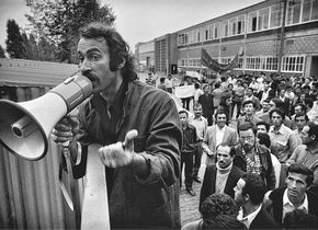Baha Targün mit Megafon am Werkstor, im Hintergrund Streikende. Aus der Serie „Ford-Streik“. Köln, 1973 / © Gernot Huber.